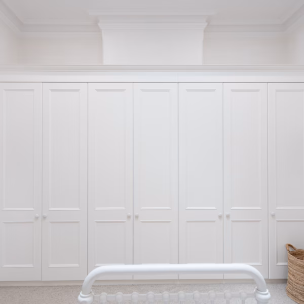 Traditional wall-to-wall Oxford wardrobe in Dulux Natural White 2-pack satin finish, custom-designed to seamlessly conceal a fireplace within the cabinetry.