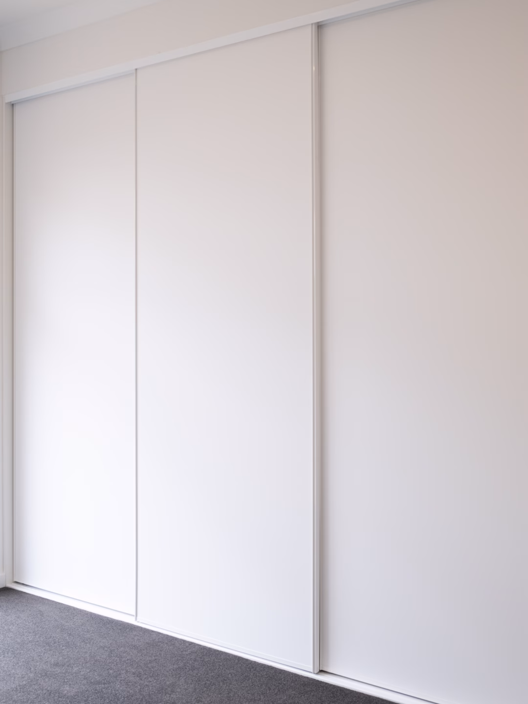 Seamless three-door Halifax sliding wardrobe in white melamine with matching slimline white frames, custom-engineered for a clean and minimalist bedroom look by Packers.