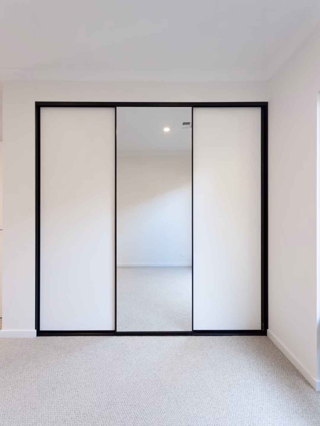 Modern three-door Halifax sliding wardrobe combining white melamine panels and full-length mirrors with slimline black frames, custom-installed by Packers.