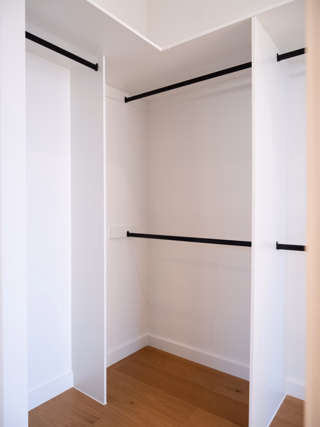 Standard walk-in robe in white melamine featuring a mix of long hanging and double hanging sections, with an accessible corner design and contrasting matte black hardware, by Packers.