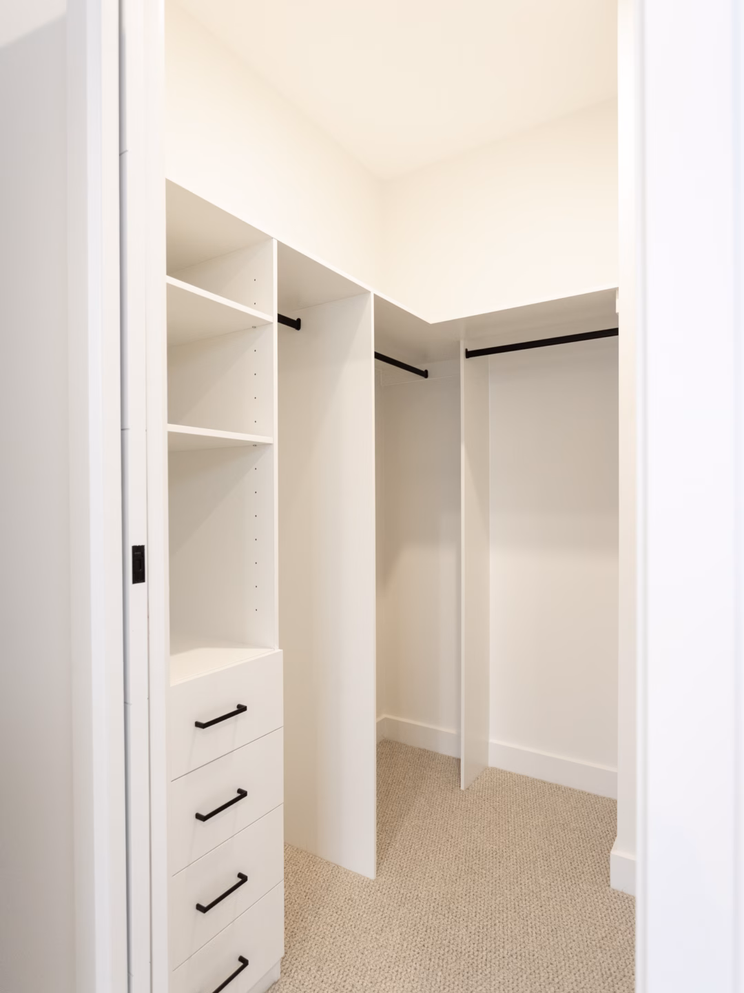Custom-built walk-in robe in white melamine featuring a classic drawer unit and contrasting matte black hardware and hanging rails, by Packers.