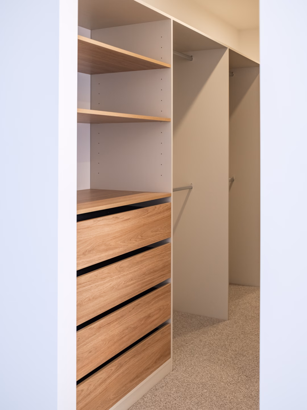 Custom-built walk-in robe featuring a mix of Polytec Greige Ravine and Prime Oak Woodmatt, showcasing integrated hanging sections alongside a central drawer unit, by Packers.